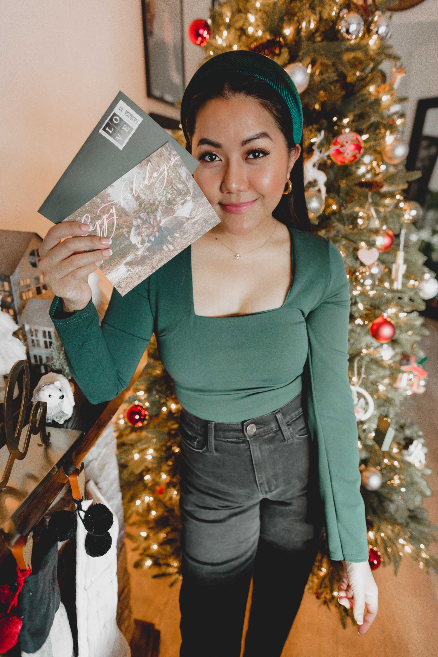 Molly larsen lifestyle blogger standing in front of a Christmas tree wearing a green dress and black jeans while holding a Christmas card Green Dress, Emerald Green Dress